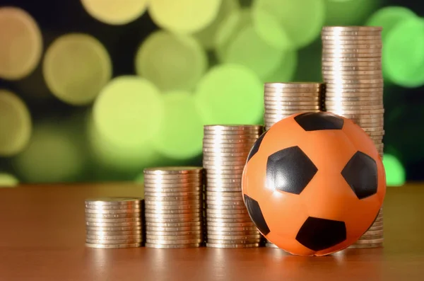 Bola de futebol e pilhas de moedas de ouro no gráfico de crescimento no fundo do bokeh borrado — Fotografia de Stock