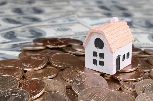 Mini house model on big coins stack on many dollar bills as background