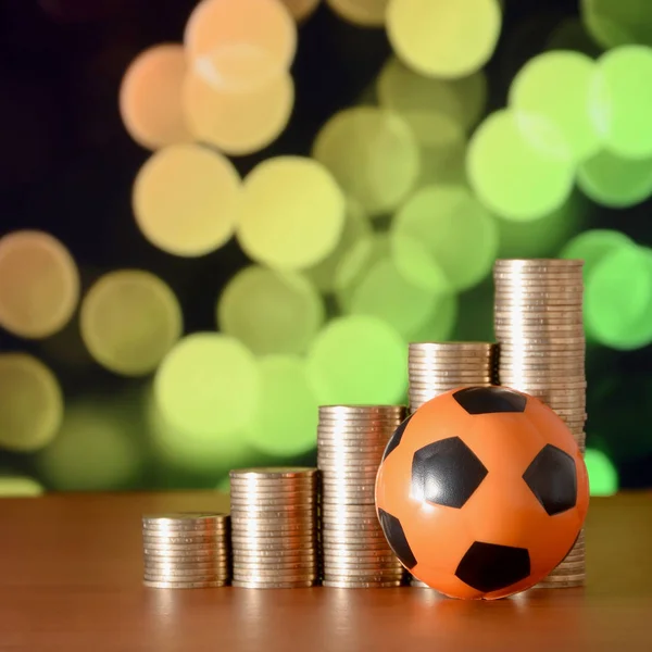 Bola de futebol e pilhas de moedas de ouro no gráfico de crescimento no fundo do bokeh borrado — Fotografia de Stock