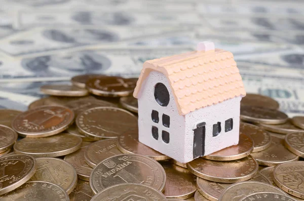 Mini house model on big coins stack on many dollar bills as background