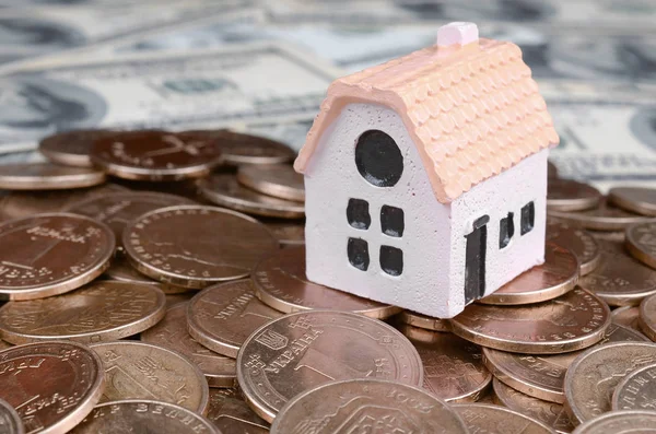 Mini house model on big coins stack on many dollar bills as background