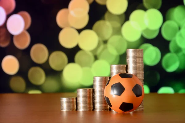 Bola de futebol e pilhas de moedas de ouro no gráfico de crescimento no fundo do bokeh borrado — Fotografia de Stock