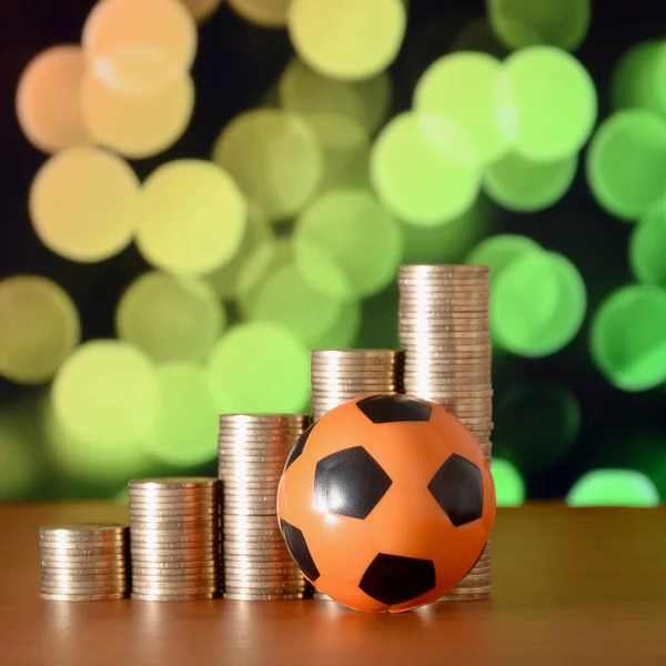 Bola de futebol e pilhas de moedas de ouro no gráfico de crescimento no fundo do bokeh borrado — Fotografia de Stock