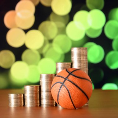 Basketball and stacks of golden coins in growth graph on the blurred bokeh background clipart