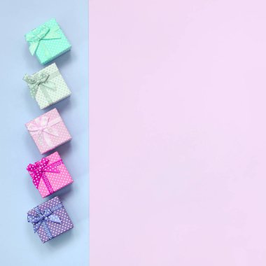 Kurdeleler ile farklı renklerde küçük hediye kutuları bir menekşe ve pembe arka plan üzerinde yatıyor
