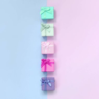 Kurdeleler ile farklı renklerde küçük hediye kutuları bir menekşe ve pembe arka plan üzerinde yatıyor