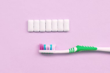 Diş fırçası ve sakız pastel pembe arka plan üzerinde yalan