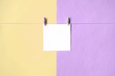 Bir kağıt parçası moda pastel sarı ve mor renklerin doku arka plan üzerinde mandal ile bir ip üzerinde asılı