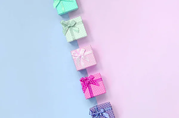 Small gift boxes of different colors with ribbons lies on a violet and pink background — Stock Photo, Image