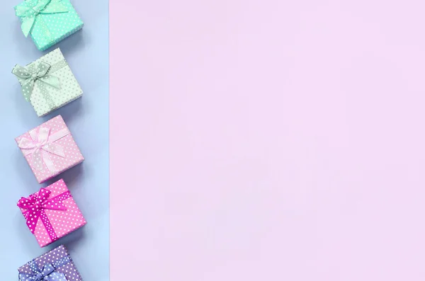Pequenas caixas de presente de cores diferentes com fitas encontra-se em um fundo violeta e rosa — Fotografia de Stock