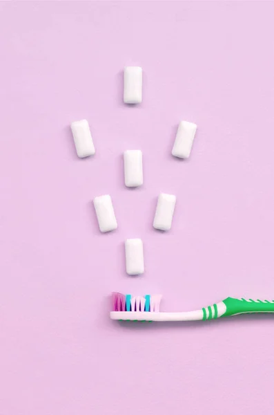 Szczoteczki do zębów i gumy do żucia leżą na pastelowe różowe tło — Zdjęcie stockowe