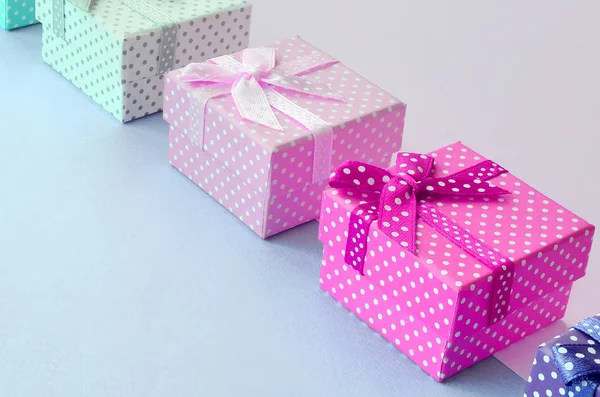 Pequeñas cajas de regalo de diferentes colores con cintas se encuentra en un fondo violeta y rosa — Foto de Stock