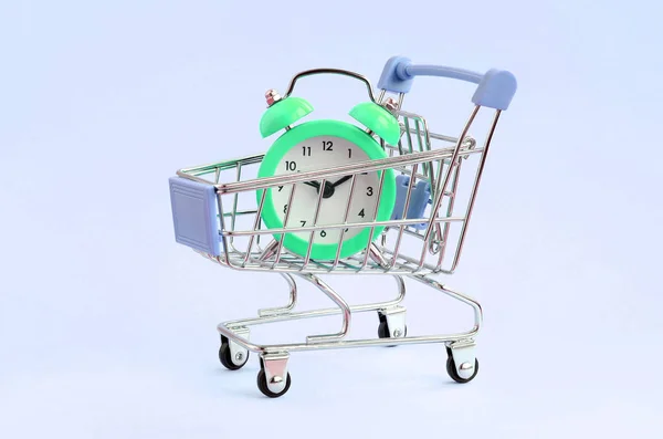 Reloj despertador verde en carro de supermercado sobre fondo azul — Foto de Stock