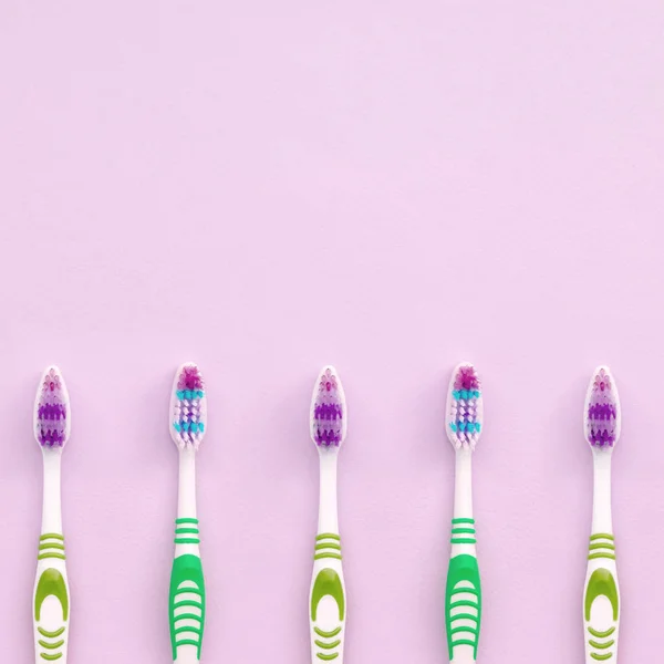 A lot of toothbrushes lie on a pastel pink background — Stock Photo, Image