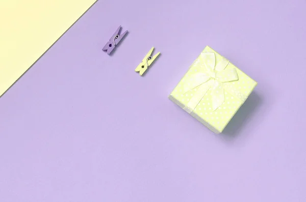 Pequena caixa de presente amarelo e dois pinos encontram-se no fundo textura de moda pastel amarelo e violeta cores papel — Fotografia de Stock