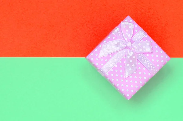 Malá růžová Dárková krabice leží na pozadí texturové tyrkysové a červené barvy papíru — Stock fotografie