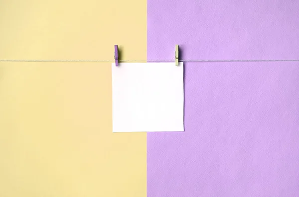 A piece of paper is hanging on a rope with pegs on texture background of fashion pastel yellow and violet colors