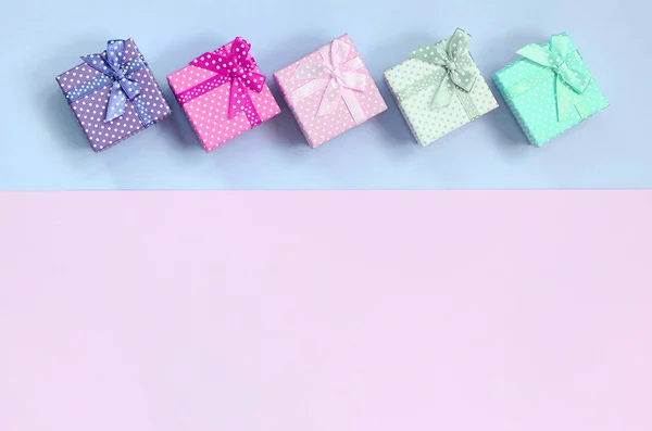 Pequenas caixas de presente de cores diferentes com fitas encontra-se em um fundo violeta e rosa — Fotografia de Stock