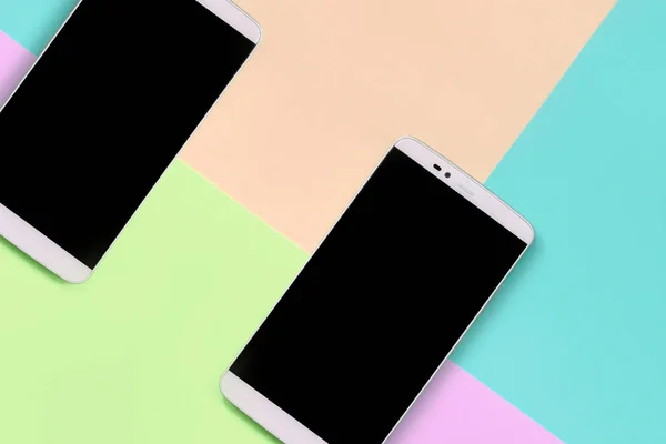 Two modern smartphones with black screens on background of fashion pastel pink, blue, coral and lime colors