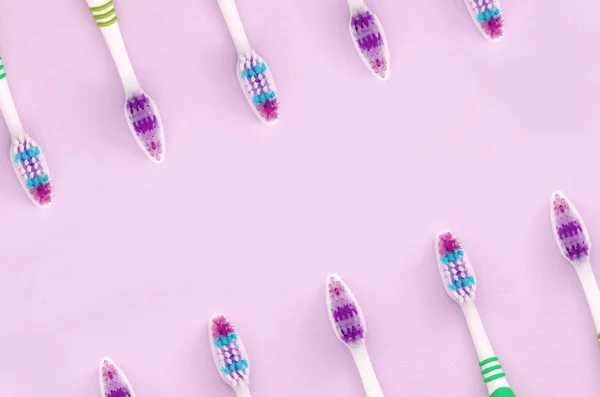 A lot of toothbrushes lie on a pastel pink background — Stock Photo, Image