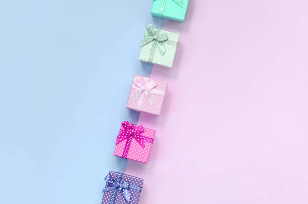 Kurdeleler ile farklı renklerde küçük hediye kutuları bir menekşe ve pembe arka plan üzerinde yatıyor — Stok fotoğraf