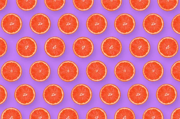 明るい紫色の背景にグレープフルーツ柑橘類のスライスのパターン — ストック写真