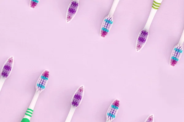 A lot of toothbrushes lie on a pastel pink background — Stock Photo, Image