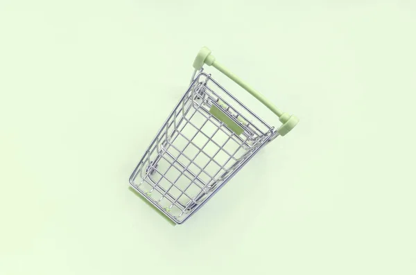 Small shopping cart lies on a lime background. Minimalism flat lay — Stock Photo, Image