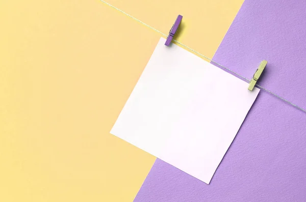 A piece of paper is hanging on a rope with pegs on texture background of fashion pastel yellow and violet colors