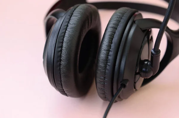 Концепція прослуховування музики. Чорні навушники лежать на рожевому фоні — стокове фото