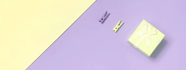 Pequena caixa de presente amarelo e dois pinos encontram-se no fundo textura de moda pastel amarelo e violeta cores papel — Fotografia de Stock