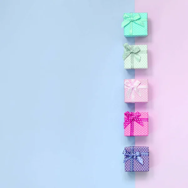 Kleine Geschenkboxen in verschiedenen Farben mit Schleifen liegt auf einem violetten und rosa Hintergrund — Stockfoto