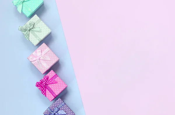 Pequeñas cajas de regalo de diferentes colores con cintas se encuentra en un fondo violeta y rosa —  Fotos de Stock