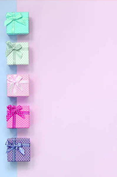 Kleine Geschenkboxen in verschiedenen Farben mit Schleifen liegt auf einem violetten und rosa Hintergrund — Stockfoto