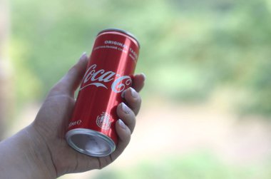 Beyaz kadın kırmızı Coca-Cola kalay yeşil bahçe arka plan ile tutar