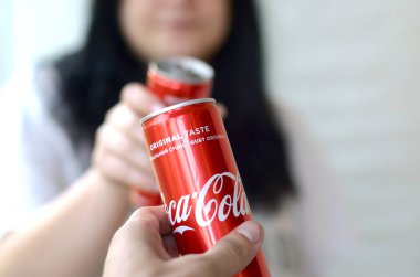 Happy woman raise Coca-Cola tin can with male friend in garage interior clipart
