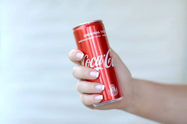 Vrouwelijke hand houdt rode Coca-Cola tin kan op witte muur achtergrond — Stockfoto