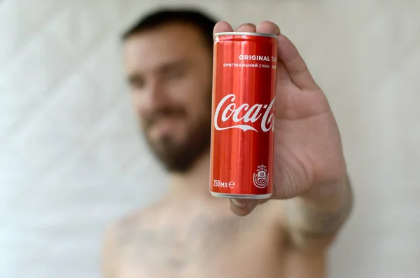 Улыбающийся мужчина представляет безалкогольную банку из-под алюминия Coca-Cola в гараже — стоковое фото