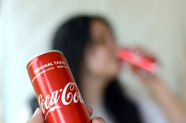 Брюнетка пьет Coca-Cola напиток в гараже интерьер и мужская рука представляет одну банку колы в фокусе — стоковое фото