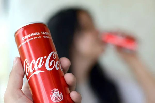 Brünette Frau trinkt Coca-Cola-Drink im Garageninneren und männliche Hand präsentiert eine Cola-Dose im Fokus — Stockfoto