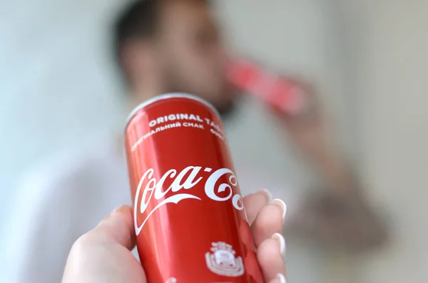 Hombre caucásico bebe bebida Coca-Cola en garaje interior y mano masculina presenta una lata de Coca Cola roja en foco — Foto de Stock