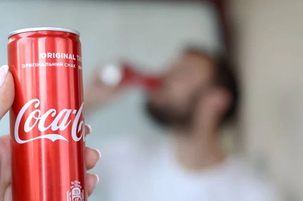 Uomo caucasico beve Coca-Cola bevanda in garage interno e mano maschile presenta una Coca cola rosso può a fuoco — Foto Stock