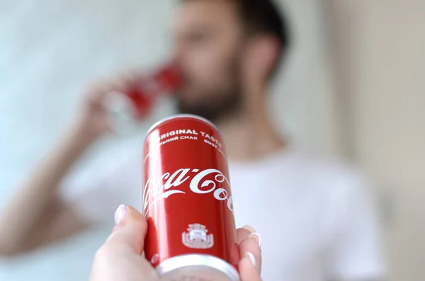 Homem caucasiano bebe bebida Coca-Cola em garagem interior e mão masculina apresenta uma lata de Coca-cola vermelha em foco — Fotografia de Stock