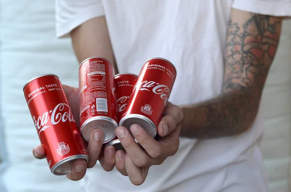 Mãos masculinas segura muitas latas de alumínio Coca-Cola não alcoólicas no interior da garagem — Fotografia de Stock