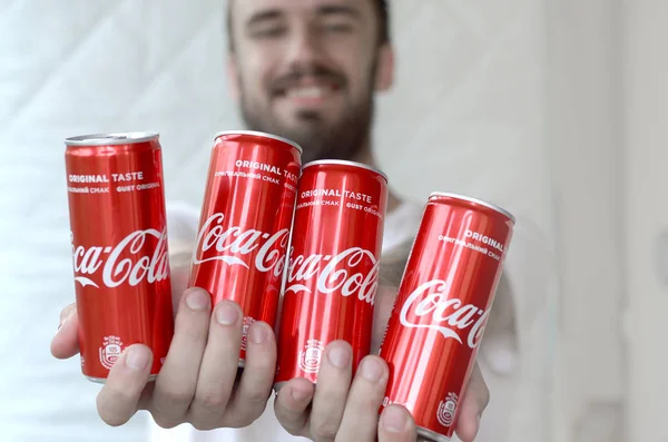 Улыбающийся мужчина держит в гараже много безалкогольных алюминиевых жестяных банок Coca-Cola — стоковое фото