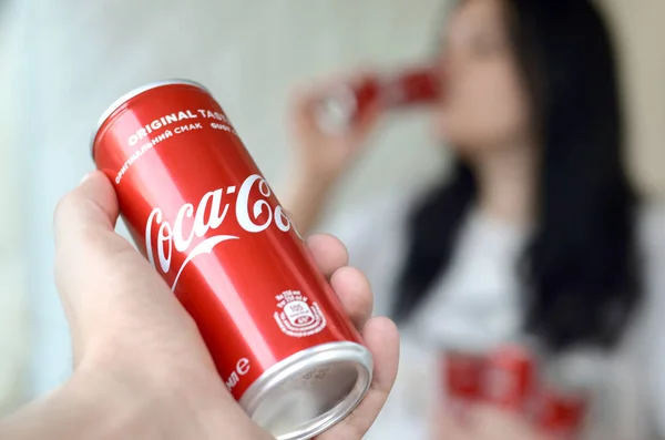 Morena mujer bebe Coca-Cola bebida en garaje interior y mano masculina presenta una cola puede en foco — Foto de Stock