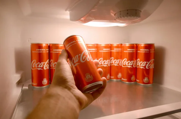 Male hand shows Coca-cola red drink can inside domestic cooler fridge full of coke cans — Stock Photo, Image