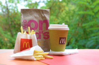 McDonald's take away paper bag and junk food on wooden table outdoors clipart