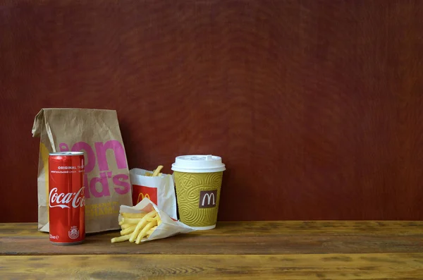 Mcdonald's ahşap masa üzerinde coca cola kutu ile kağıt torba ve patates kızartması götürmek — Stok fotoğraf