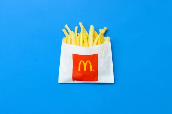 Papas fritas McDonald 's en una pequeña bolsa de papel sobre fondo azul brillante —  Fotos de Stock